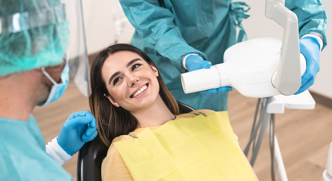 Woman in yellow bib receiving dental examination from dentist in surgical gloves and mask.