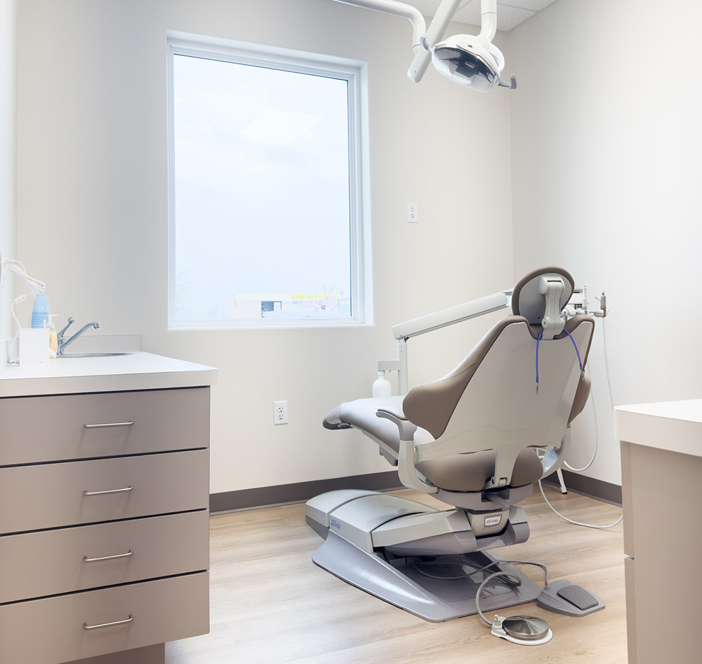 Modern dental operatory with empty treatment chair, overhead light, and clinical equipment in bright office.