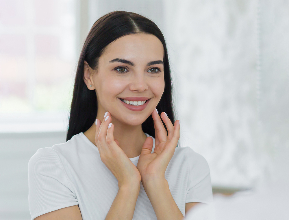 Young woman smiling while touching her face in bright, modern dental office setting.