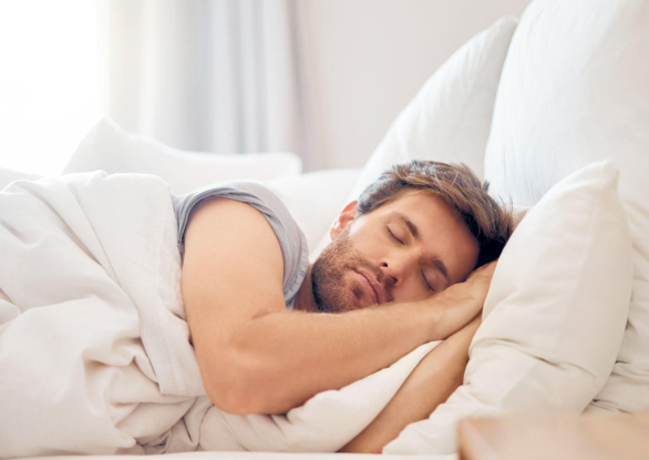 Man sleeping peacefully in bed with white pillows and bedding.
