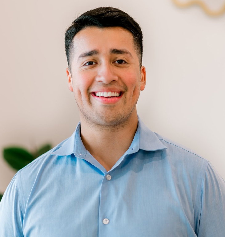 Professional headshot of smiling man in light blue shirt against neutral background at dental office.