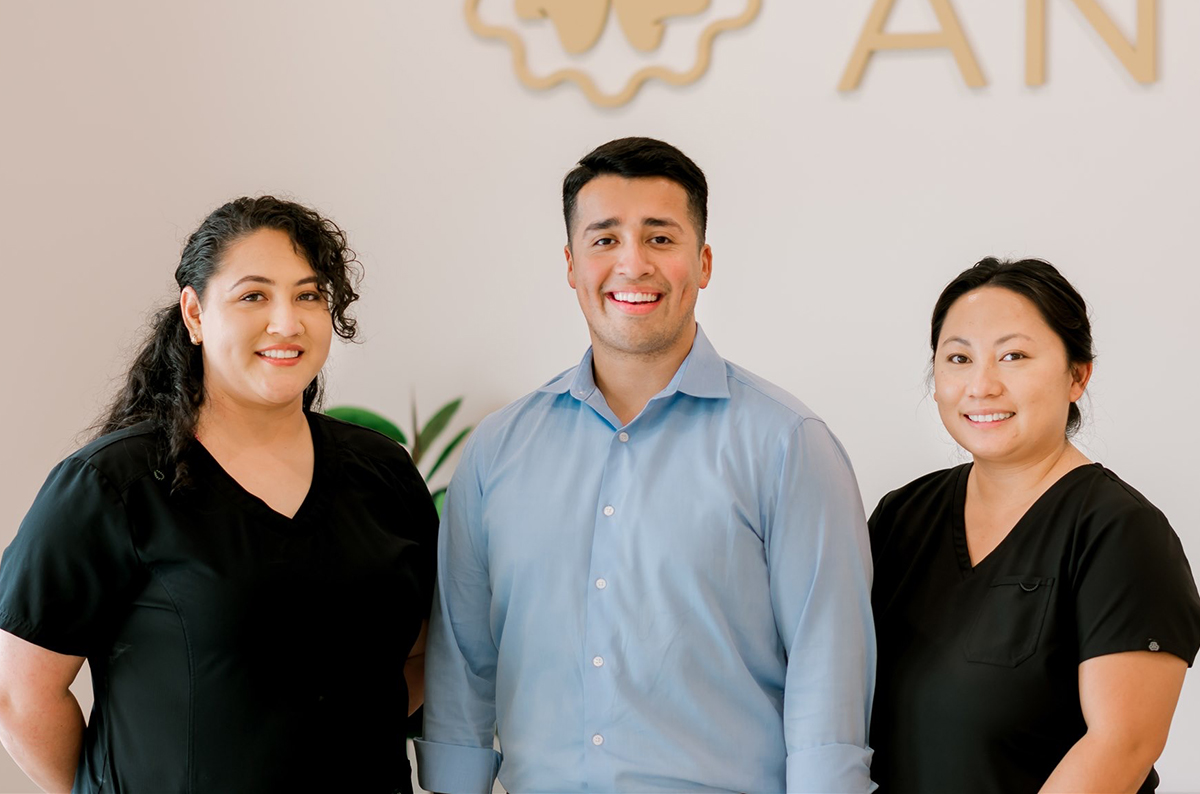 Three dental professionals smiling at camera in front of Dental Wellness of Anna branded backdrop.