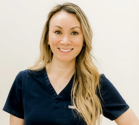 Professional headshot of smiling woman in dark scrubs against neutral background.