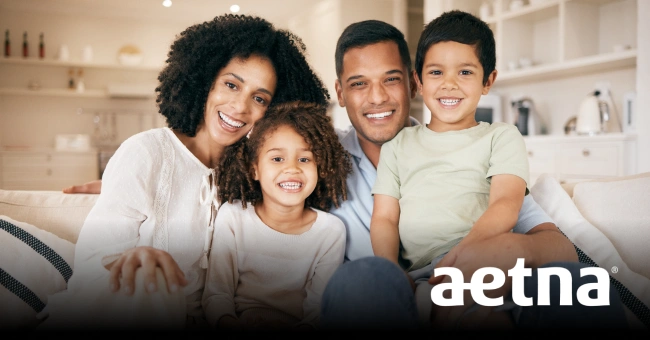 Happy family of four smiling together in bright, modern kitchen with Aetna logo.