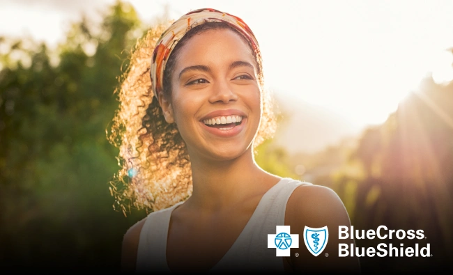 Smiling woman outdoors in natural sunlight with Blue Cross Blue Shield dental wellness logo.