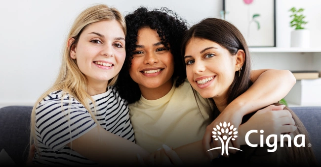 Three smiling women posing together indoors with Cigna dental logo visible.