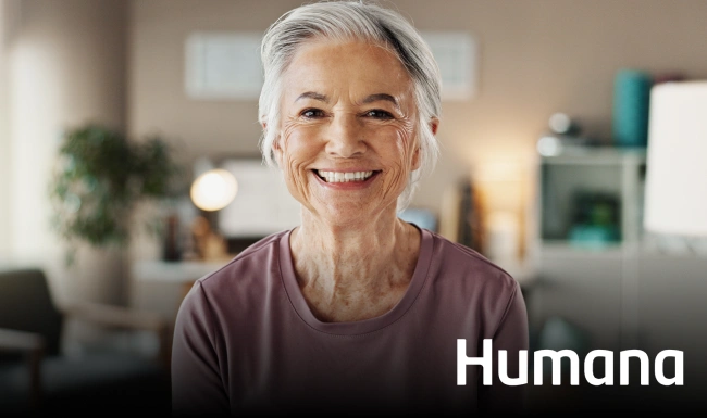 Smiling senior woman in modern dental office setting with Humana branding visible.
